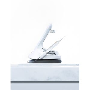 The LX 16 PLUS, a white handheld device with a pointed tip, sits on its docking station.